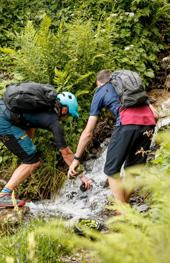 Compedalrunde im Kristeinertal Zwei Männer füllen ihre Trinkflaschen an einem kleinen Bachlauf entlang der Compedalrunde im Kristeinertal.