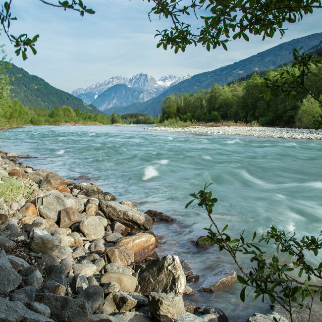 Iselbucht Aufnahme vom steinigen Ufer der Isel mit Blick auf den schnell fließenden Fluss und die Berge im Hintergrund an einem sonnigen Tag.