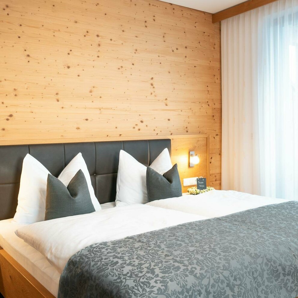 Doppelbett mit Bettbezug in weiß und grau und hölzernes Getäfel auf der Wand