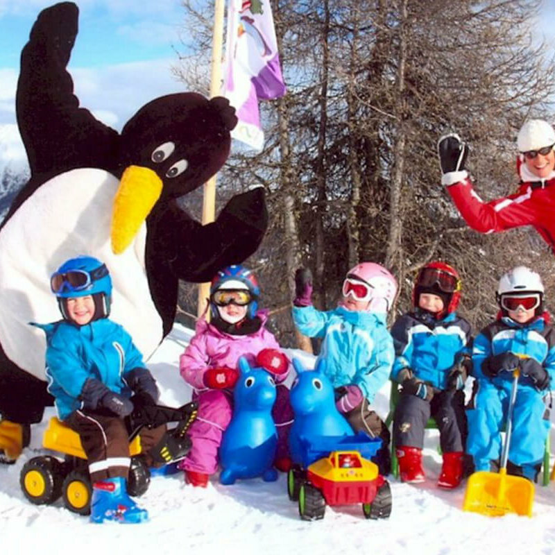Wintersportschule Hochpustertal Kinder mit ihrem Skilehrer und einem Pinguin-Maskottchen im Skizentrum Hochpustertal