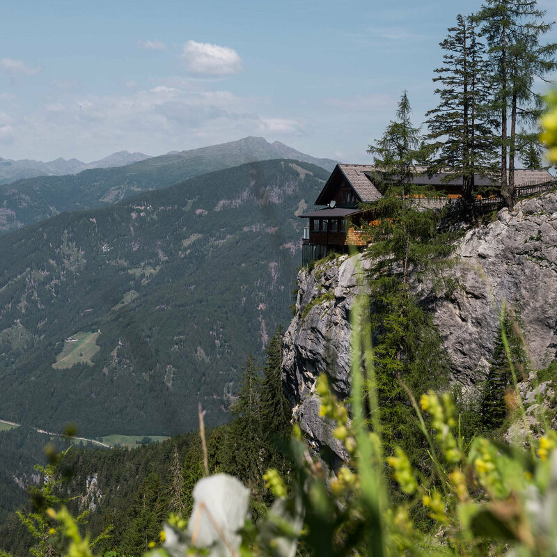 Dolomitenhuette Die Dolomittenhütte steht auf einem Plateau vor einem Abgrund in sommerlicher Landschaft.