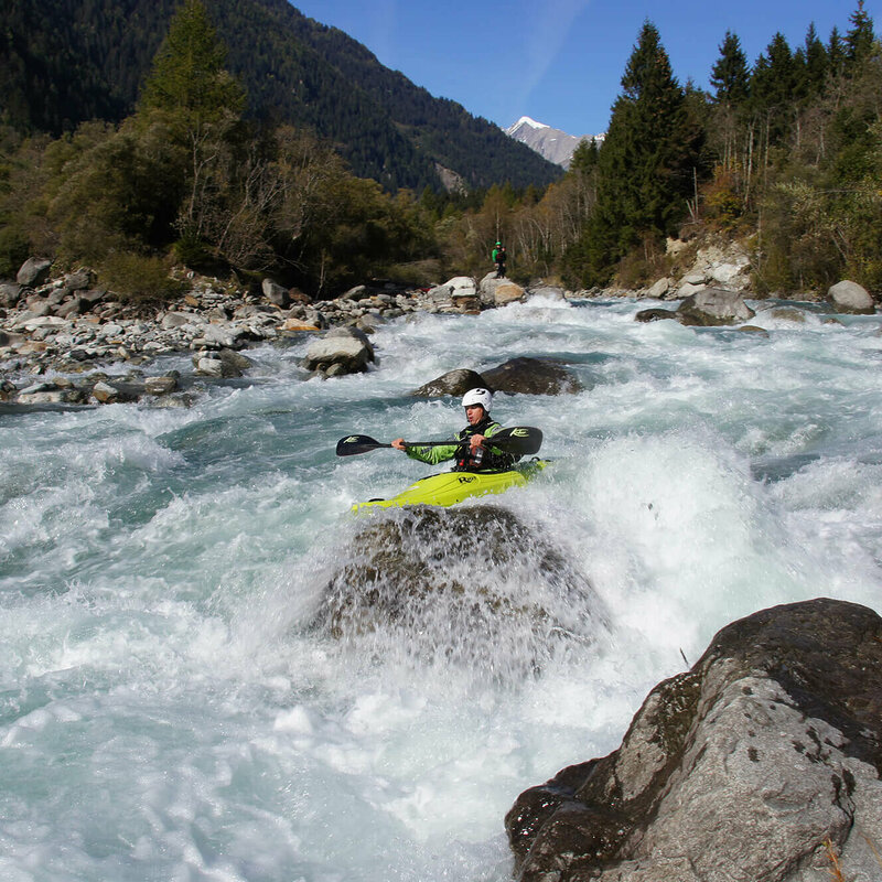 Kajak Ein Kajakfahrer inmitten des Wildwasserflusses Isel in Osttirol, dahinter ist Wald und eine Bergspitze.