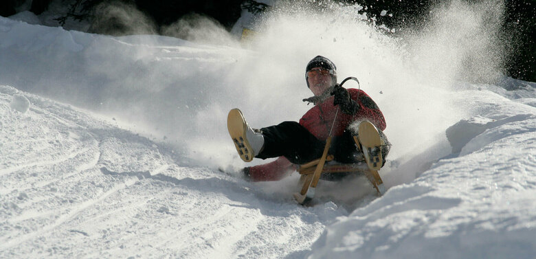 Rodel Leckfeldalm Rodelbahn Da staubt der Pulverschnee, als der Rodler die Kurve einer Rodelbahn nimmt. Ein natürlcher Schneewall begrenzt die Bahn.